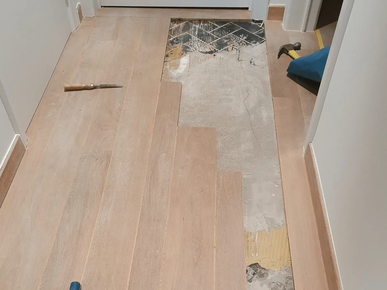 Herstelling van een plankenvloer: beschadigde planken uitgezaagd, de ondervloer zichtbaar