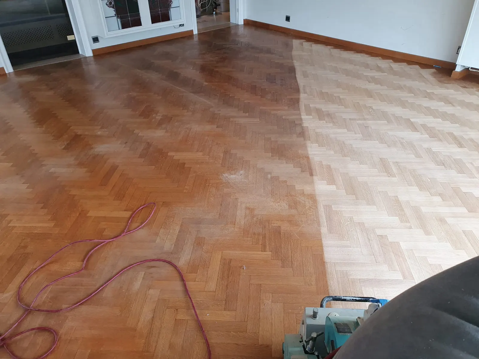 Visgraatparket tijdens het herschuren: links nog de oude lak, rechts het geschuurde hout