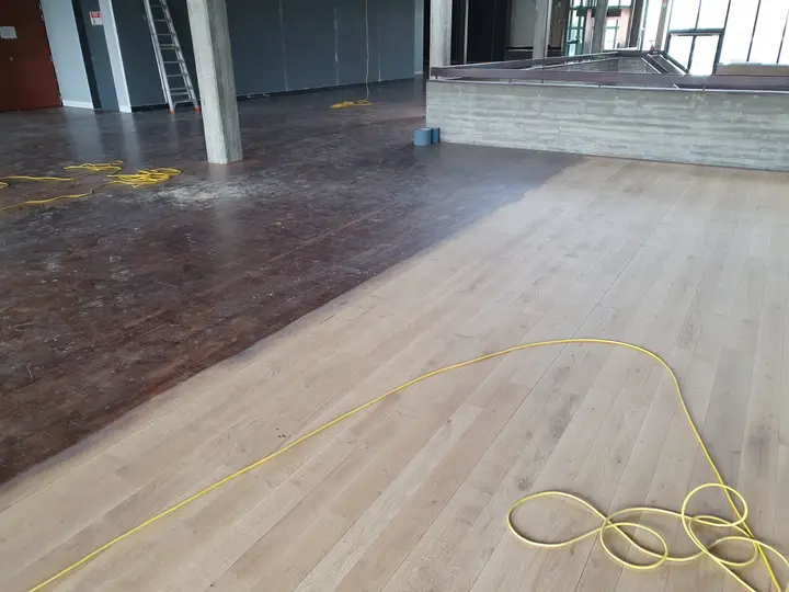 Een grote zaal met de oude donkere vloer naast het opgeschuurde deel